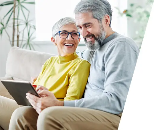 senior male and female sitting on a couch using an iPad