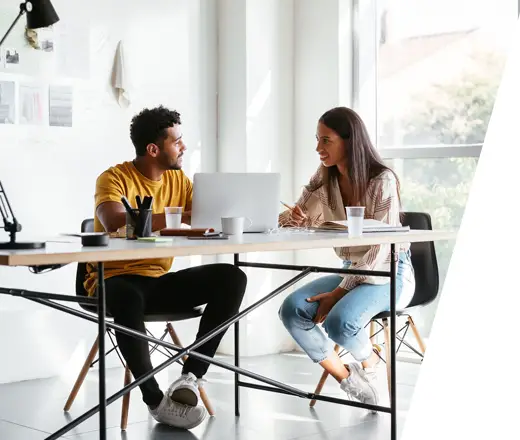 young male and female working on a laptop at a large table