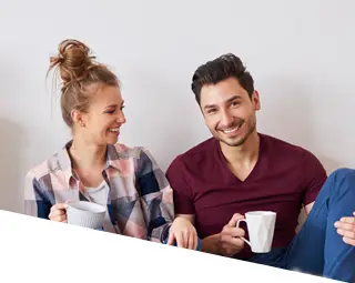 happy male and female sitting on the floor drinking a cup of coffee with their dog