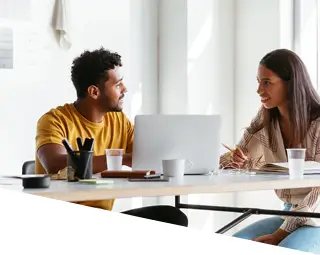 young male and female working on a laptop at a large table